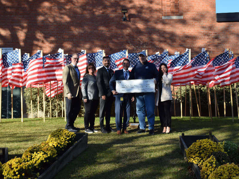 administrators holding giant check in front of standing american flags