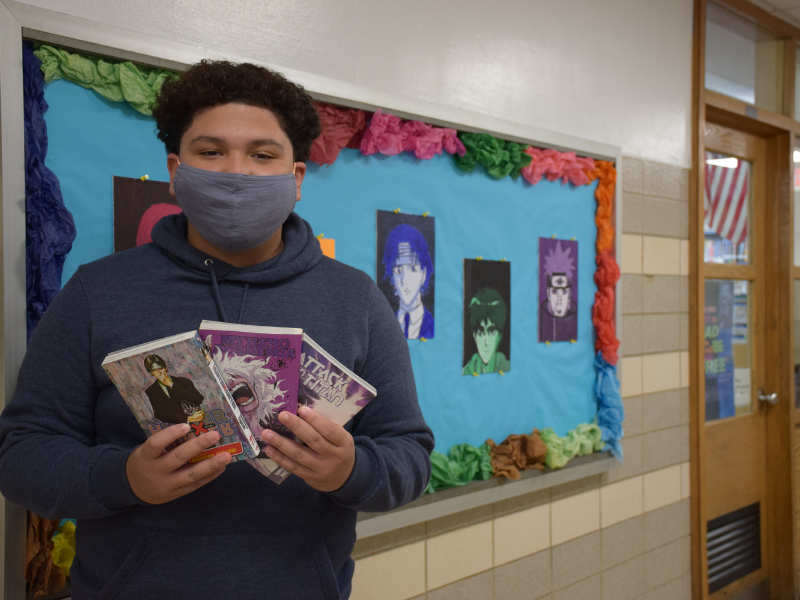 William Cruz in front of his artwork with anime books. 