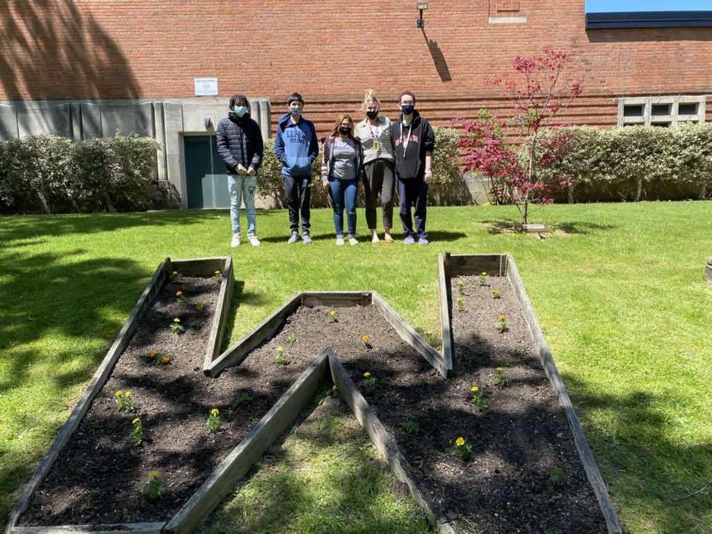 High school students with Ms. Sheila Dempsey outside after planting flowers in front of the school building.